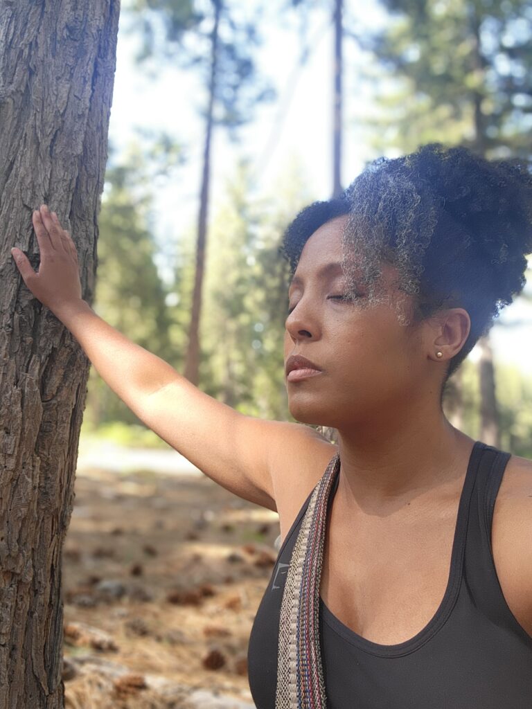 Black woman touching a tree.